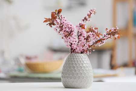 Vase with beautiful blossoming branches on table in room