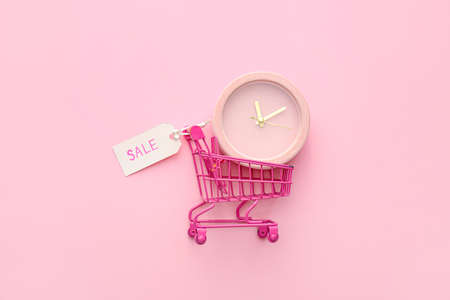 Alarm clock in small shopping cart on pink background, top view