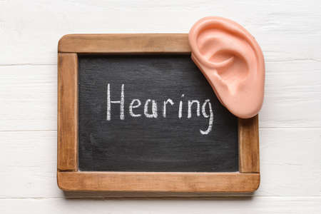 Chalk board with word HEARING and ear model on white wooden backgroundの写真素材