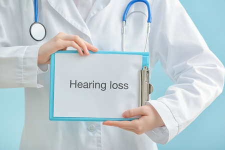 Female doctor holding clipboard with text HEARING LOSS on color backgroundの写真素材