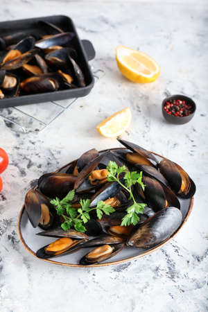 Plate and baking dish with tasty mussels on light background