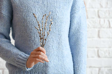 Woman holding willow branches near brick wall, closeup