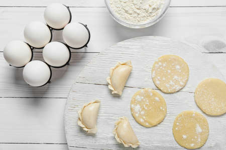 Composition with raw dumplings on light wooden background