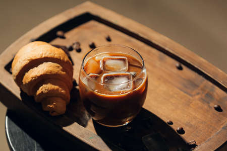 Glass of tasty iced coffee with milk and croissant on tableの写真素材