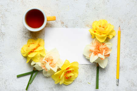 Cup of tea, beautiful daffodils and blank card on light background