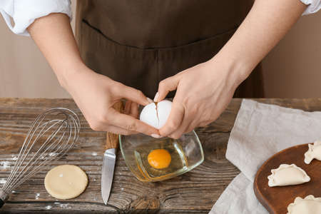 Woman breaking egg into bowl on kitchen table, closeup