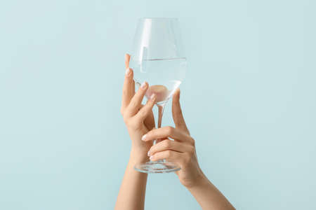 Woman with beautiful manicure holding glass of water on color backgroundの写真素材