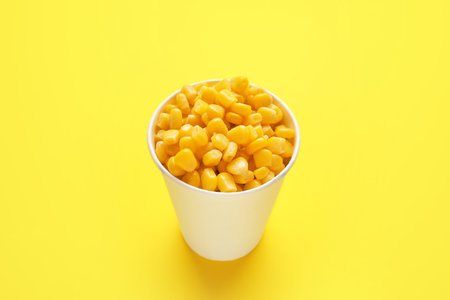Paper cup of corn kernels on color background