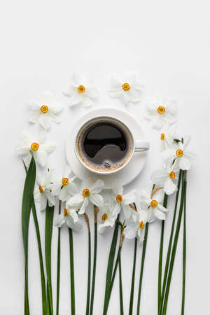 Cup of coffee and beautiful narcissus flowers on white background