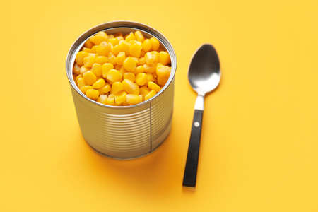 Opened tin can of corn kernels and spoon on color backgroundの写真素材