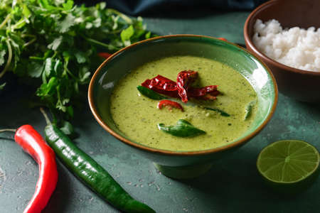 Bowl of tasty green chicken curry and ingredients on color background
