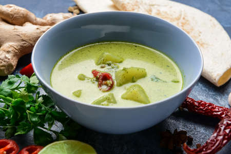 Bowl of tasty green chicken curry and ingredients on color background, closeupの写真素材
