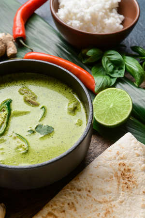 Bowl of tasty green chicken curry and ingredients on table, closeup