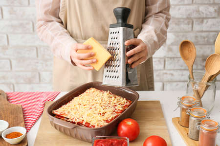 Woman adding cheese in baking dish with tasty tomato lasagna at kitchen table, closeupの写真素材