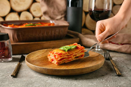 Woman putting piece of tasty tomato lasagna on plateの写真素材