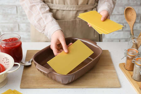 Woman preparing tasty lasagna at table in kitchen, closeup