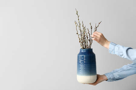 Female hands and vase with willow branches on light backgroundの写真素材