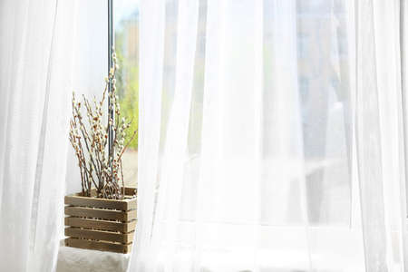 Wooden box with willow branches on windowsill
