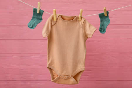 Baby clothes hanging on rope against color wooden backgroundの写真素材