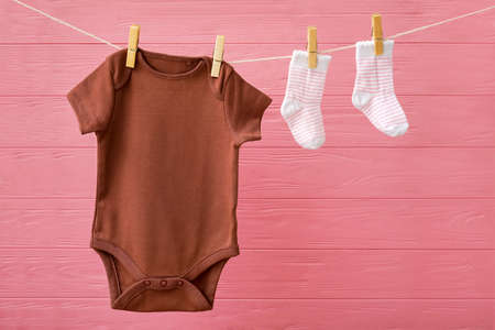 Baby clothes hanging on rope against color wooden backgroundの写真素材
