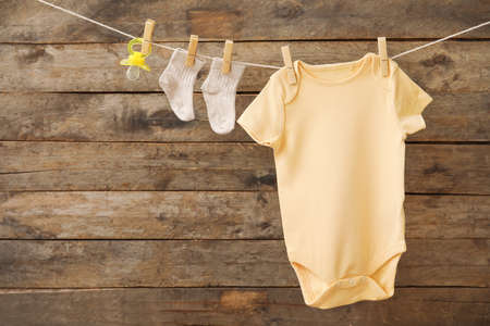 Baby clothes and pacifier hanging on rope against wooden backgroundの写真素材