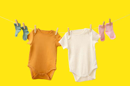 Baby clothes hanging on rope against color backgroundの写真素材