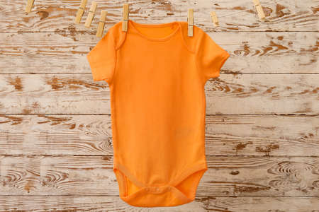 Baby clothes hanging on rope against light wooden background