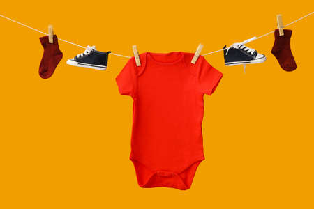 Baby clothes and shoes hanging on rope against color backgroundの写真素材