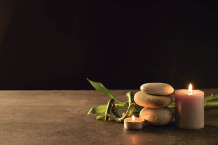 Spa stones with burning candle and bamboo branch on table against black backgroundの写真素材