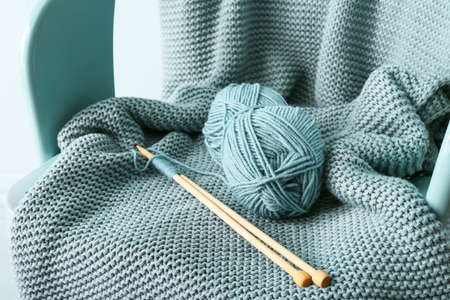 Knitting yarn, needles and plaid on chair, closeup