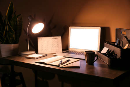 Modern workplace with computer and glowing lamp near color wallの写真素材