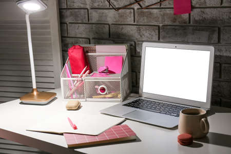 Stylish workplace with modern laptop and lamp in the evening