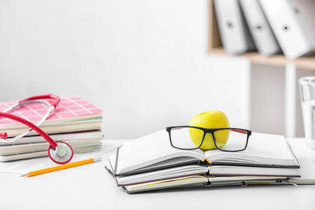 Stack of books with eyeglasses and apple on table
