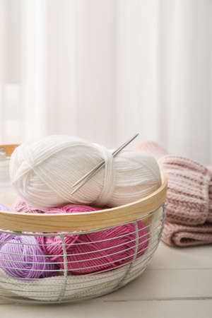 Basket with knitting yarn and needles on wooden table, closeup