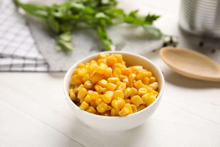 Bowl with corn kernels on light wooden background, closeup