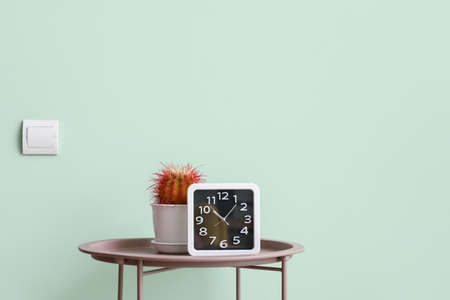 Clock and cactus on table near color wall