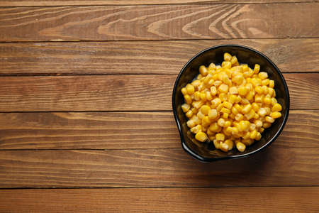Bowl with corn kernels on wooden background