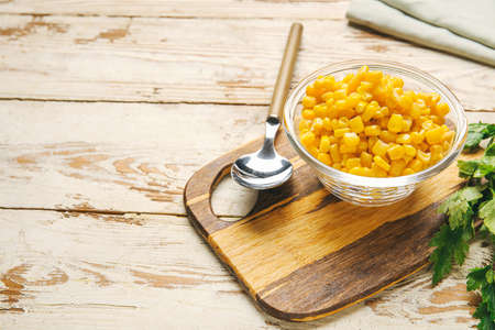 Bowl with corn kernels and parsley on light wooden background, closeup