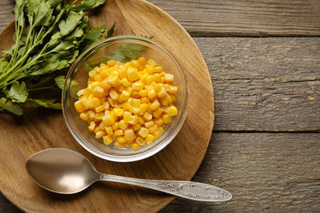 Bowl with corn kernels and parsley on wooden background