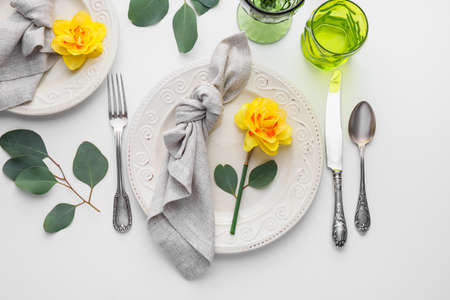 Beautiful table setting with narcissus flowers on white background