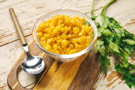 Bowl with corn kernels and parsley on light wooden background, closeupの写真素材