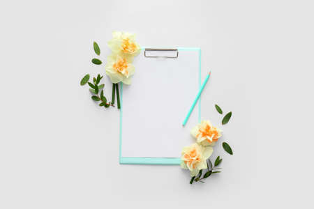Beautiful daffodils and clipboard with blank paper sheet on white backgroundの写真素材