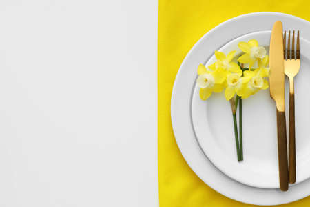 Beautiful table setting with narcissus flowers on white background