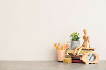 Wooden mannequin, books and stationery on table near color wall