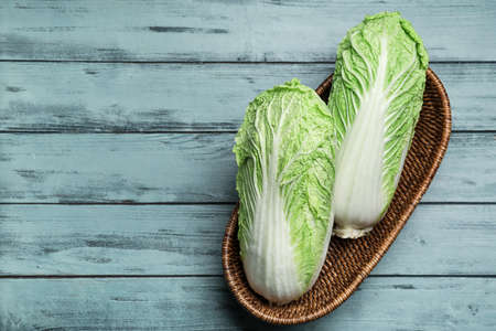 Basket with fresh chinese cabbage on color wooden background
