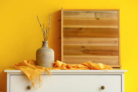 Vase with willow branches and mirror on chest of drawers in roomの写真素材