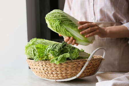 Woman with fresh chinese cabbage in basket on table, closeupの写真素材