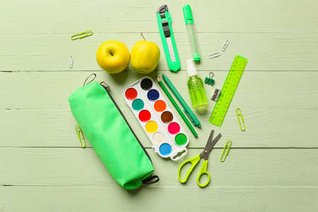 Pencil case, stationery, bottle of sanitizer and apples on color wooden background