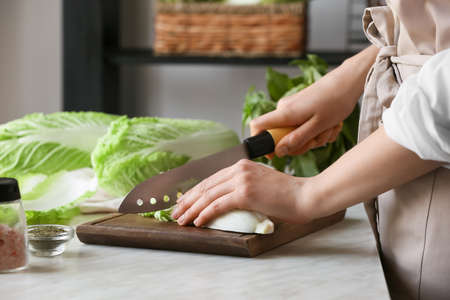 Woman cutting fresh chinese cabbage on table, closeupの写真素材