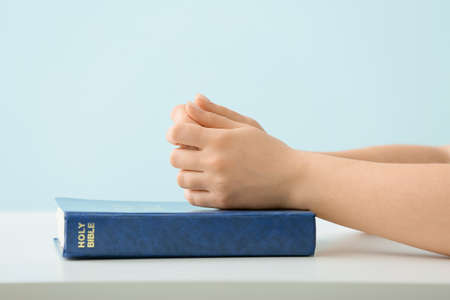 Woman praying with Holy Bible at table against blue backgroundの写真素材